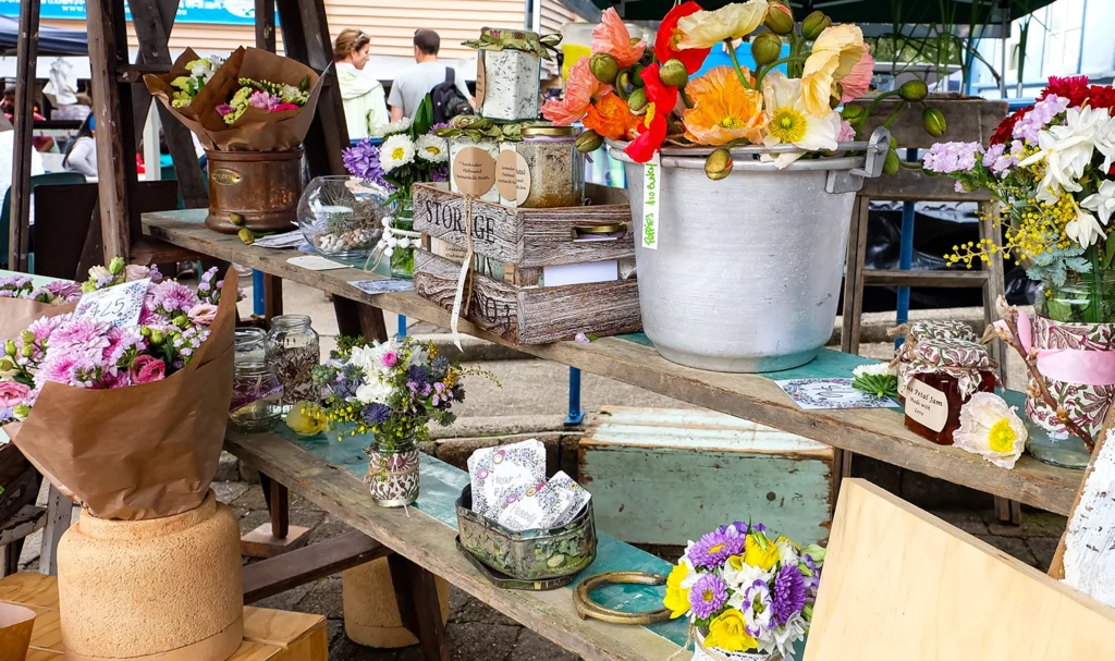 Flowers and various antiques on a wooden display in a vendor's booth at an outdoor market.