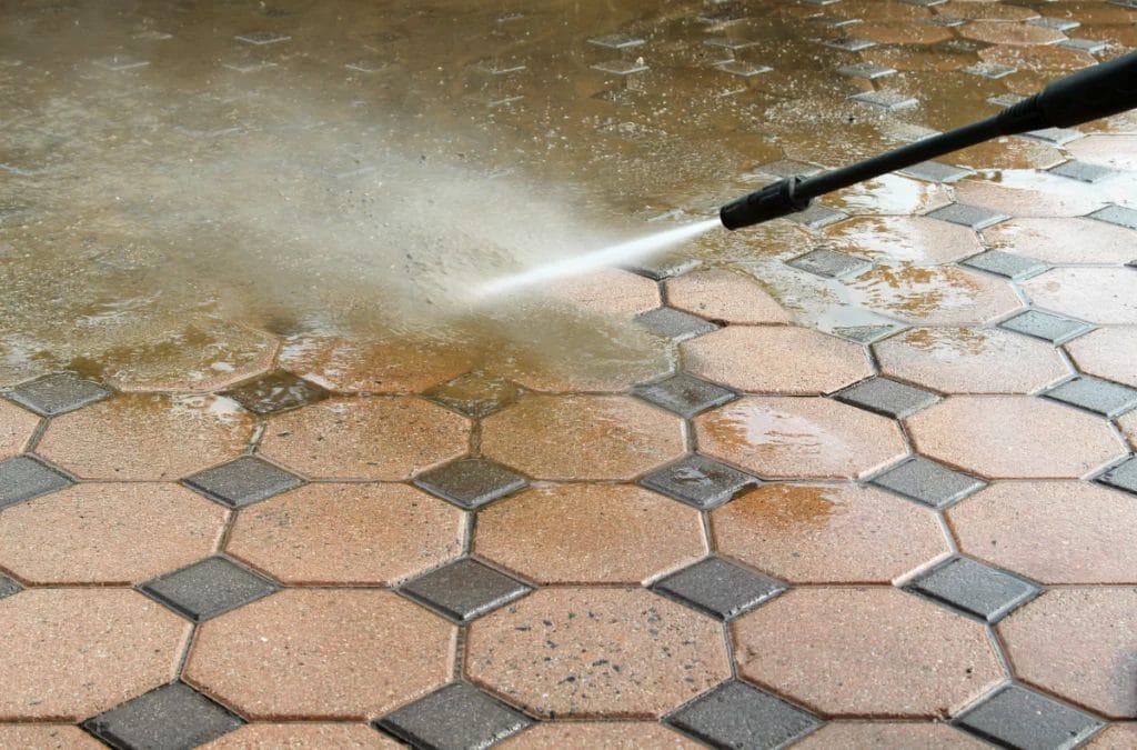 Close-up of pressure washer cleaning red-brown paving stones.