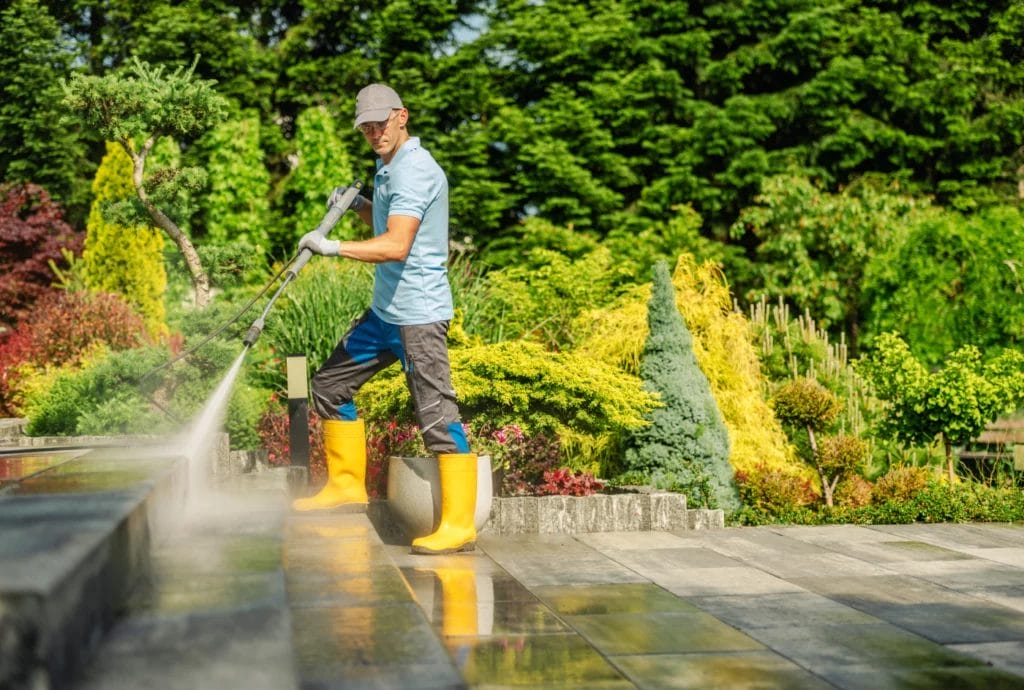 Man in yellow boots power washing a large garden patio.