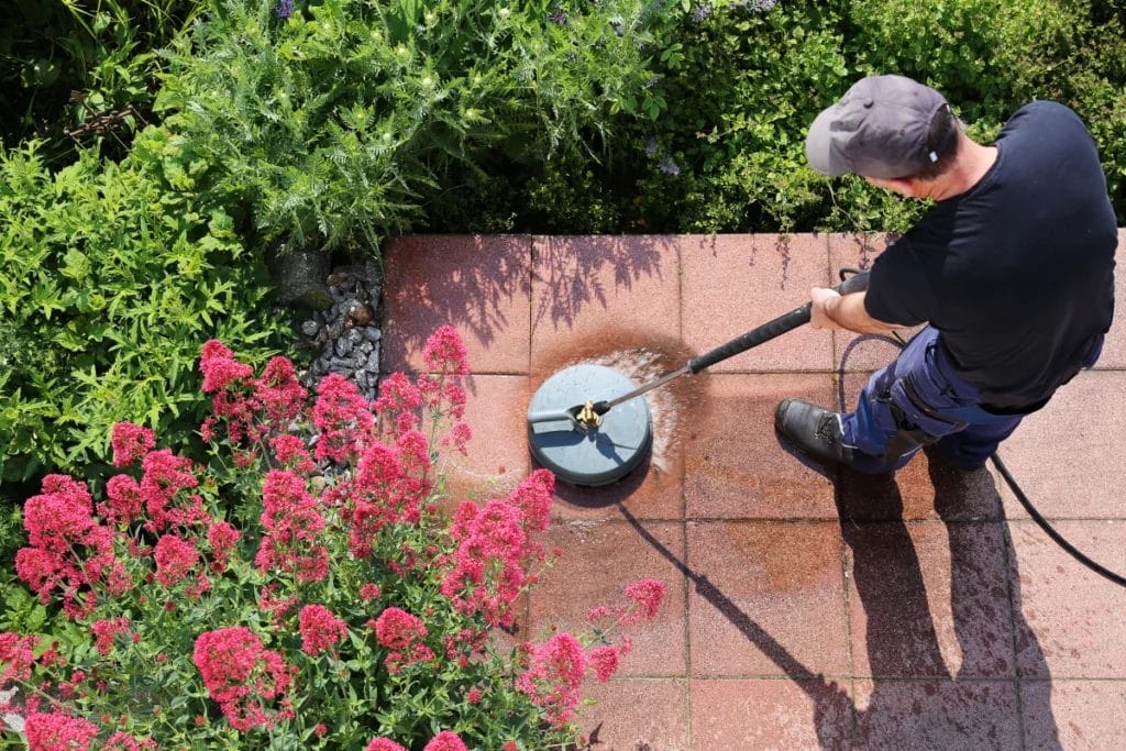 Person using a circular pressure washing tool to clean a garden patio.