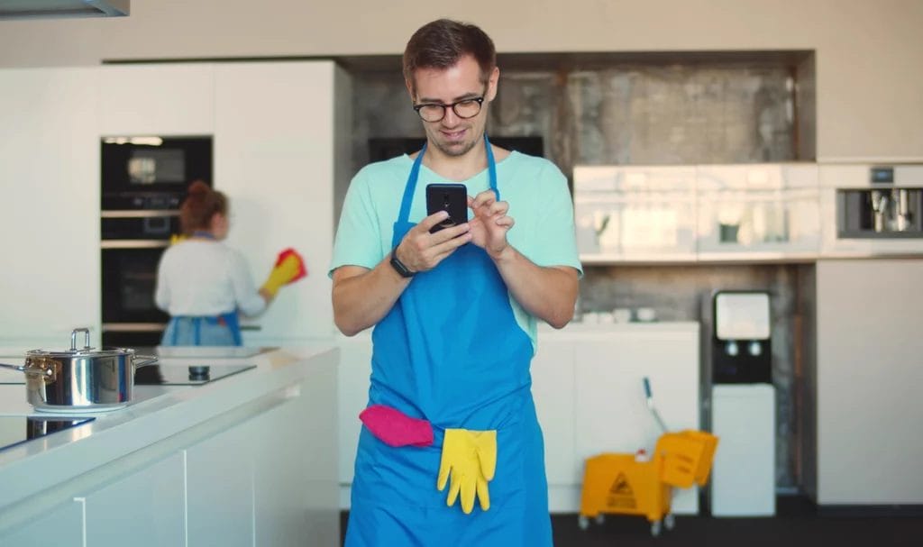 A cleaner using smartphone standing in modern home kitchen.