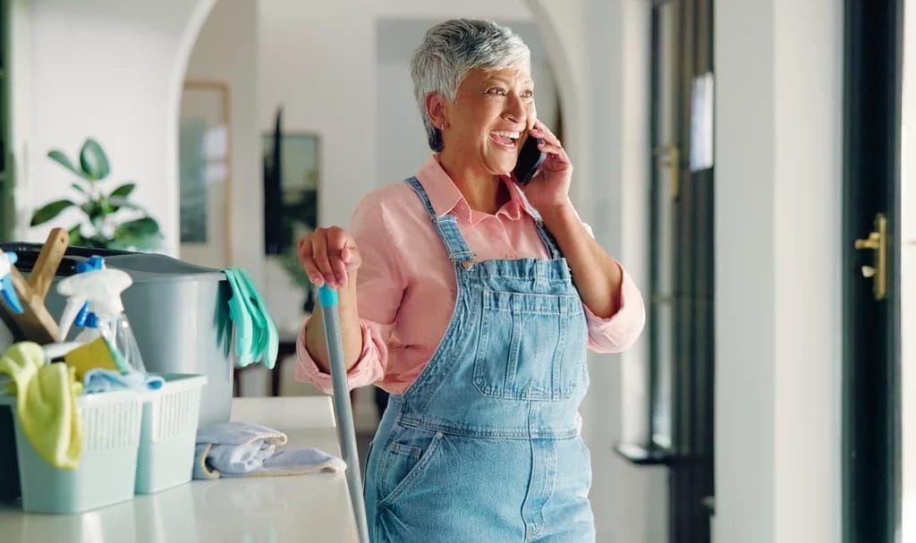 Housekeeper happily talking on phone while cleaning a home.