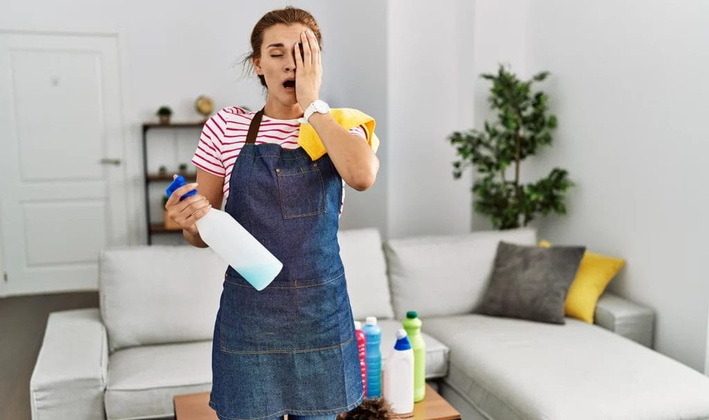 A housekeeper holds her hand up to her left eye after accidentally spraying cleaning product in her eye. Her mouth is agape in pain.