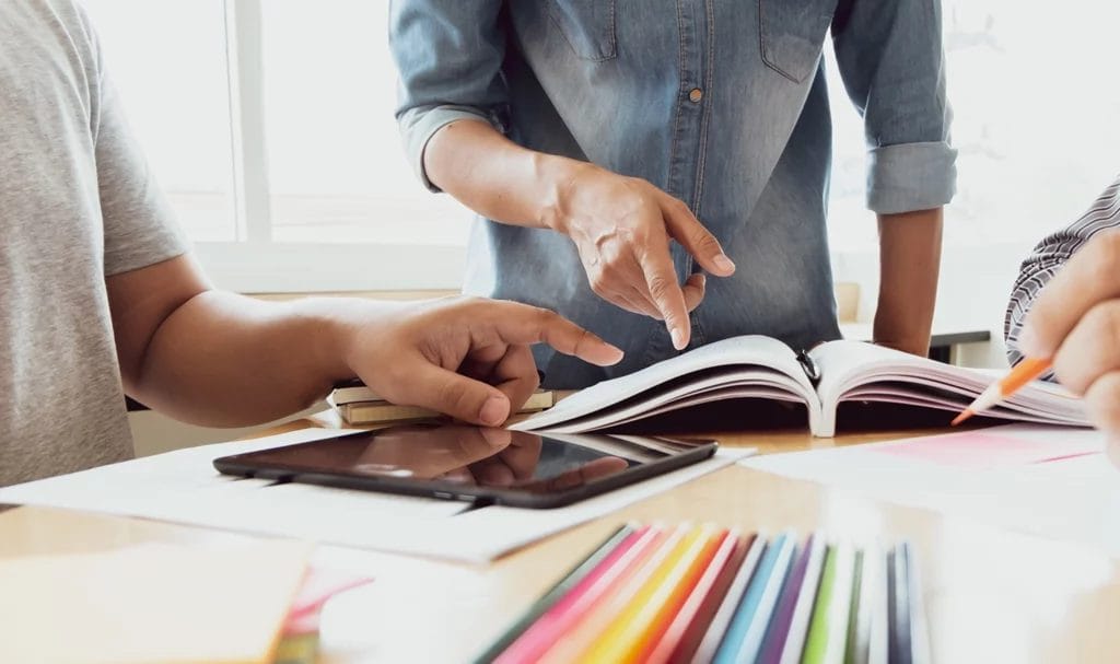 Close-up of a mentor leading a discussion with students. Books and educational materials are on the table around them.