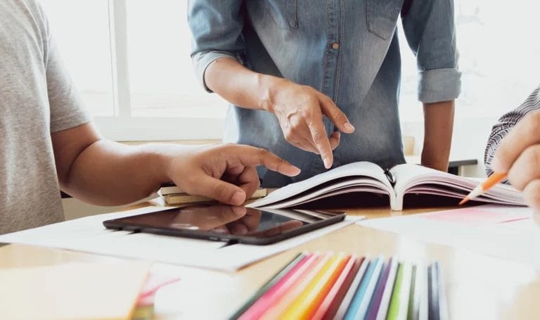 Close-up of a mentor leading a discussion with students. Books and educational materials are on the table around them.