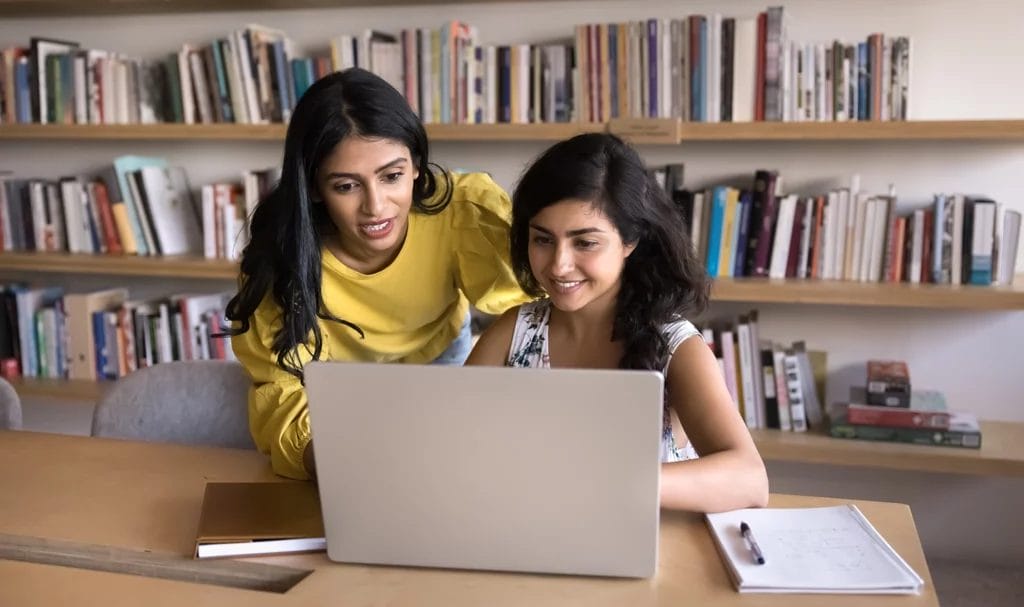 Academic consultant helping online student as she walks her through a form on her laptop in a library.