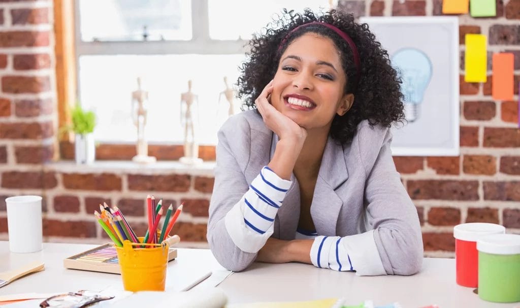 Smiling female educational consultant at desk surrounded by colorful school supplies.