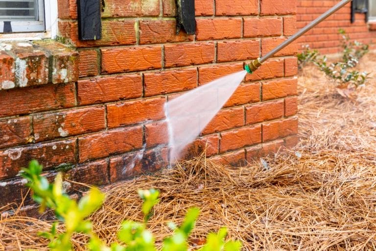 Pressure washer nozzle cleaning the side of a red brick building.