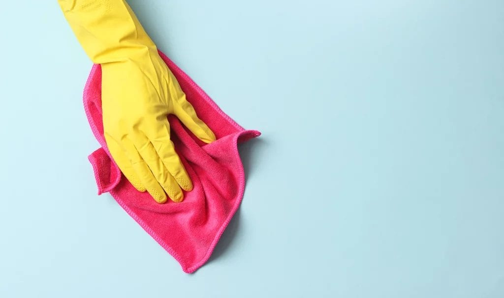 A close up look at a cleaner wearing a yellow rubber glove using a red cleaning rag to wipe down a light blue surface.