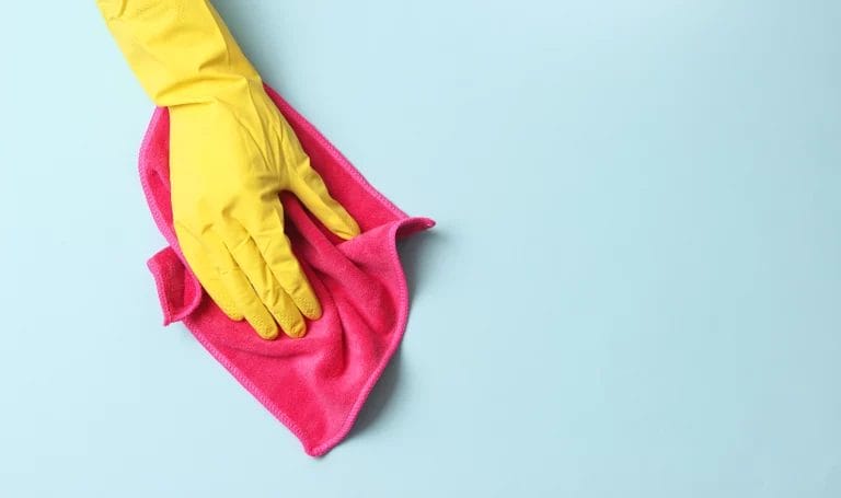 A close up look at a cleaner wearing a yellow rubber glove using a red cleaning rag to wipe down a light blue surface.