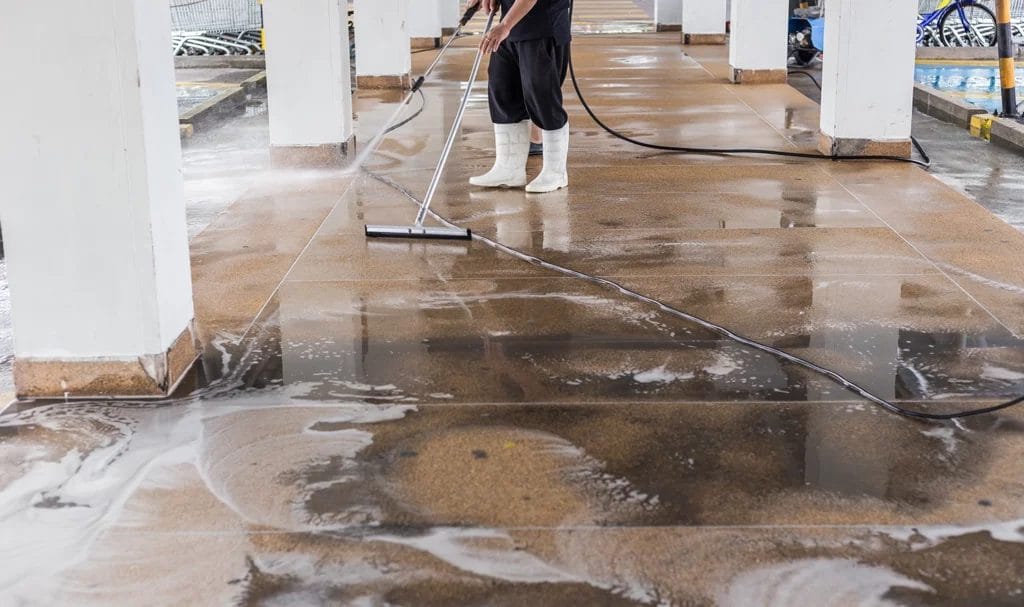 A commercial cleaner is using a sponger to clear soapy debris from the area being pressure washed.