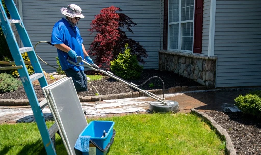 A pressure washer is using a special tool to scrub the front brick walkway of a home clean.