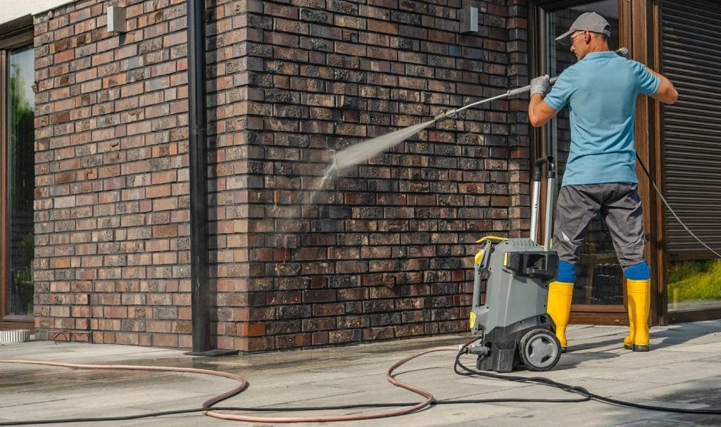 A professional cleaner is pressure washing the brick exterior of a home.