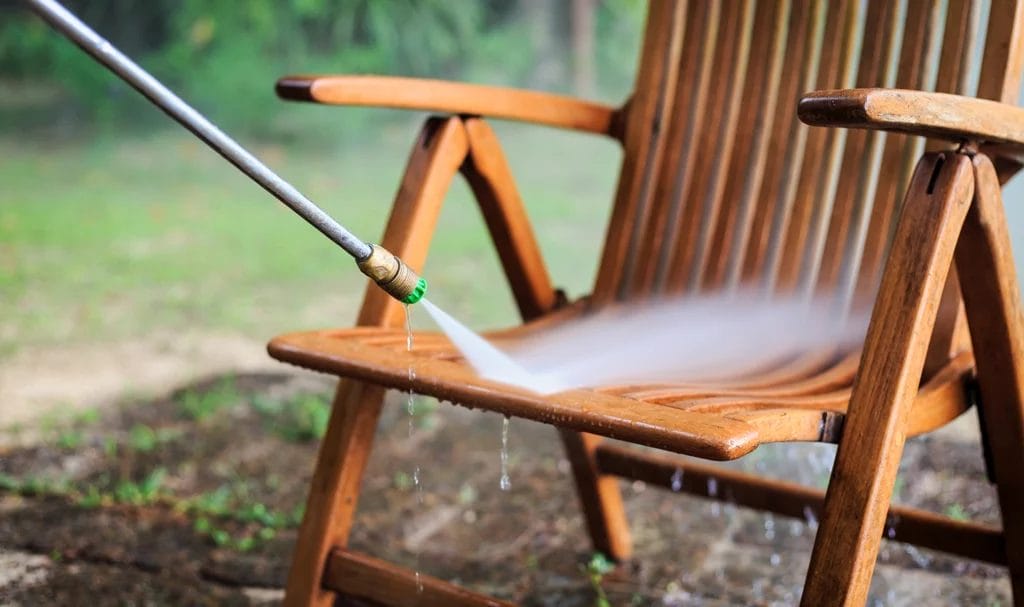 Close-up look of an outdoor wooden patio chair being cleaned with a pressure washer.