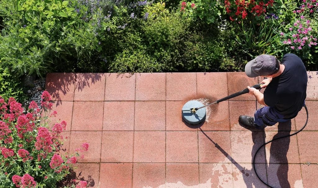 Overhead view of a professional cleaner using a special pressure washng tool to scrub a brick patio clean.