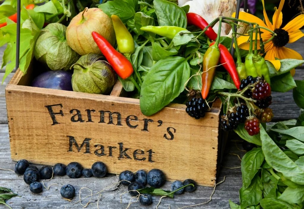 Wooden crate of herbs, peppers, and berries with a stamped "Farmers Market" label with vintage font