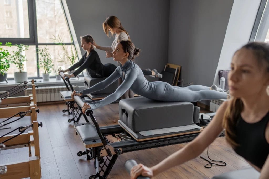 A small group Pilates class performing an exercise on the Reformers with the instructor's assistance.