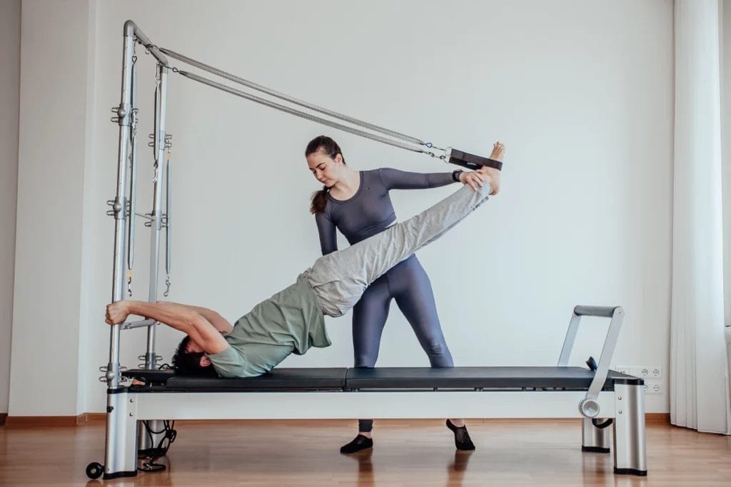 A Pilates instructor assists a client with an exercise on the Cadillac Reformer machine.