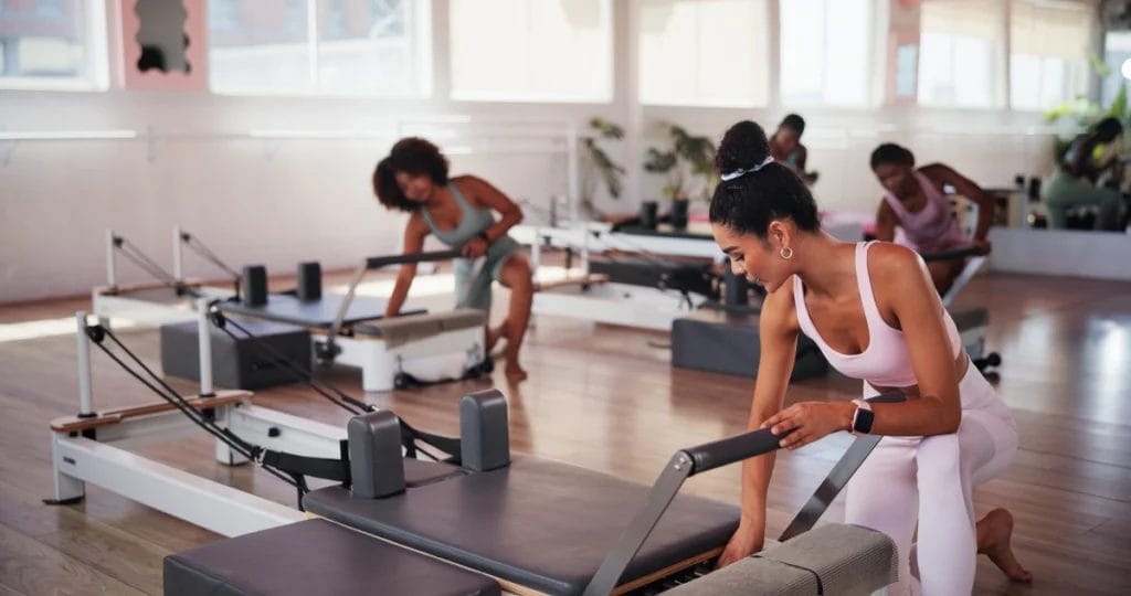 People in a Pilates class adjust their Reformer machines.