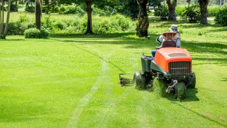 Man cuts grass with riding lawnmower.