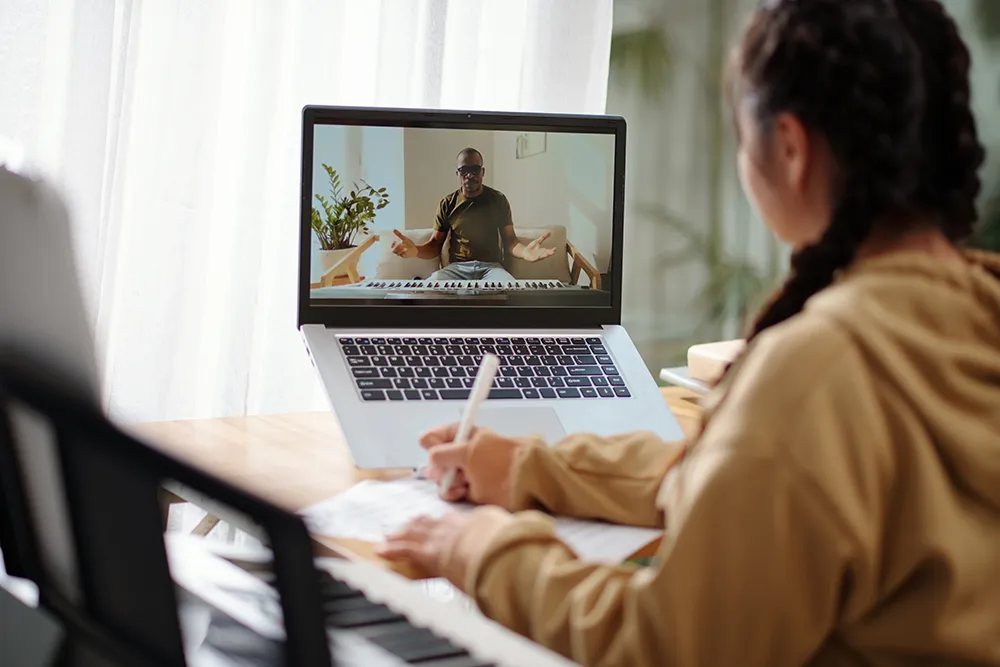 Piano student meeting with online music teacher through a laptop.