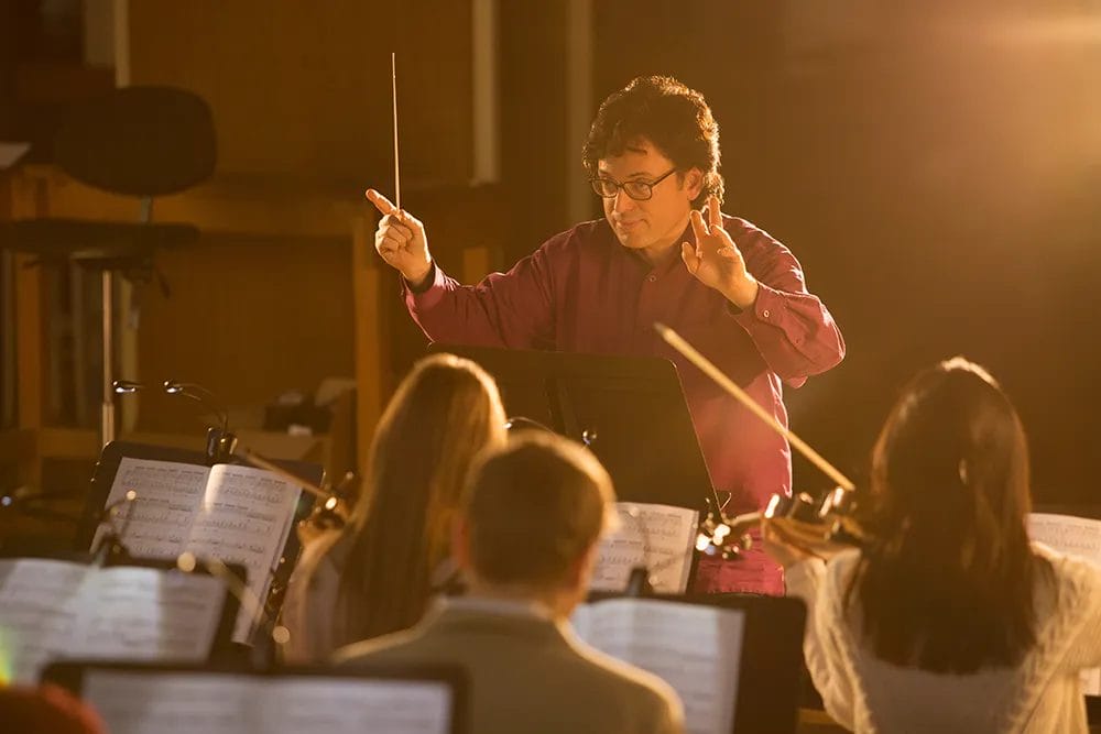 School band teacher conducts the band on stage during a performance