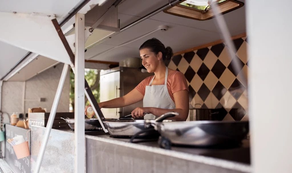 A food truck owner smiling as she prepares her pan with oil to begin making orders for the day.