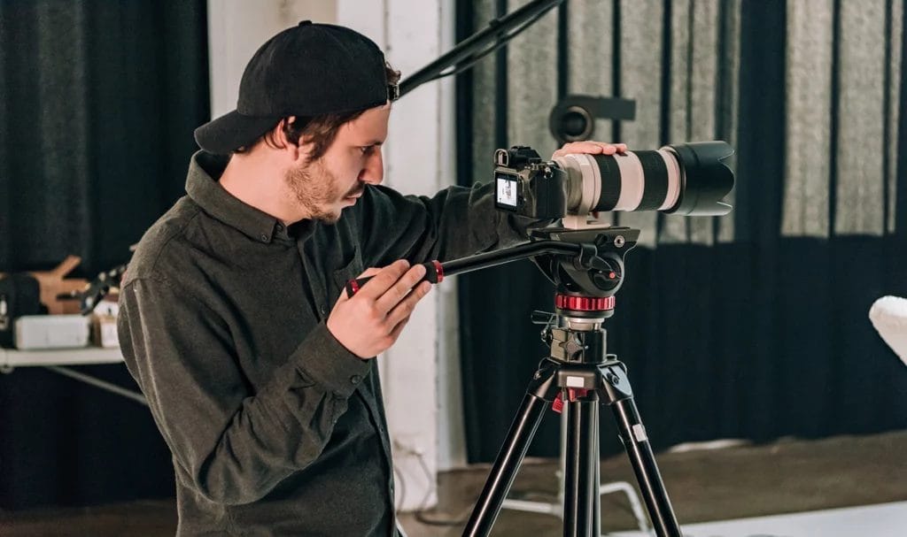 A videographer carefully panning a camera on a tripod to capture a scene in a studio.