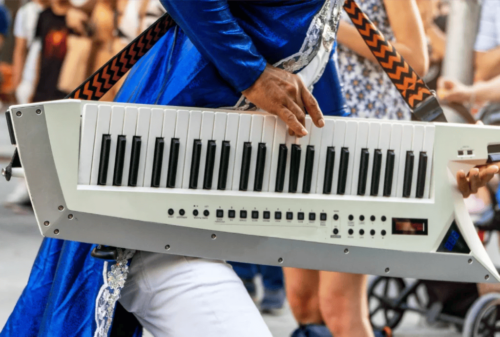 Close-up of a musician in a blue outfit playing a white keytar during a parade or street performance.