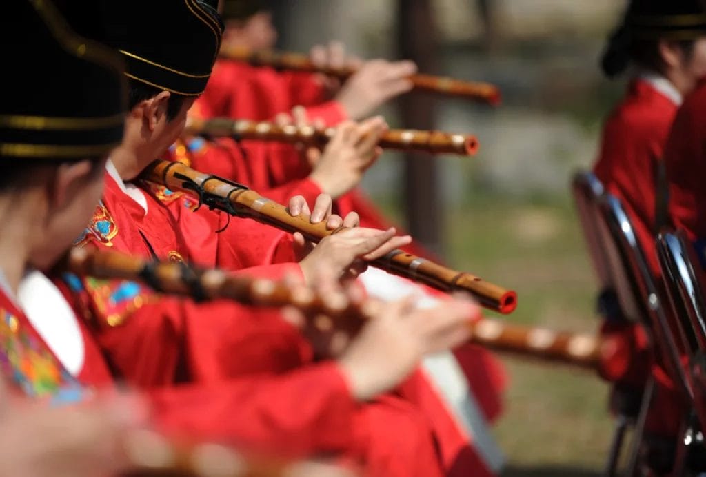 A group of musicians in red uniforms playing wooden flutes during a traditional marching band performance.