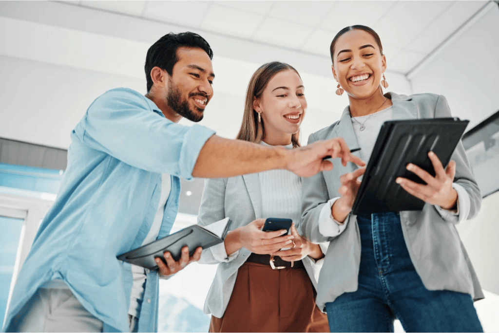 Group of smiling professionals in a casual office point to a tablet while discussing strategy.