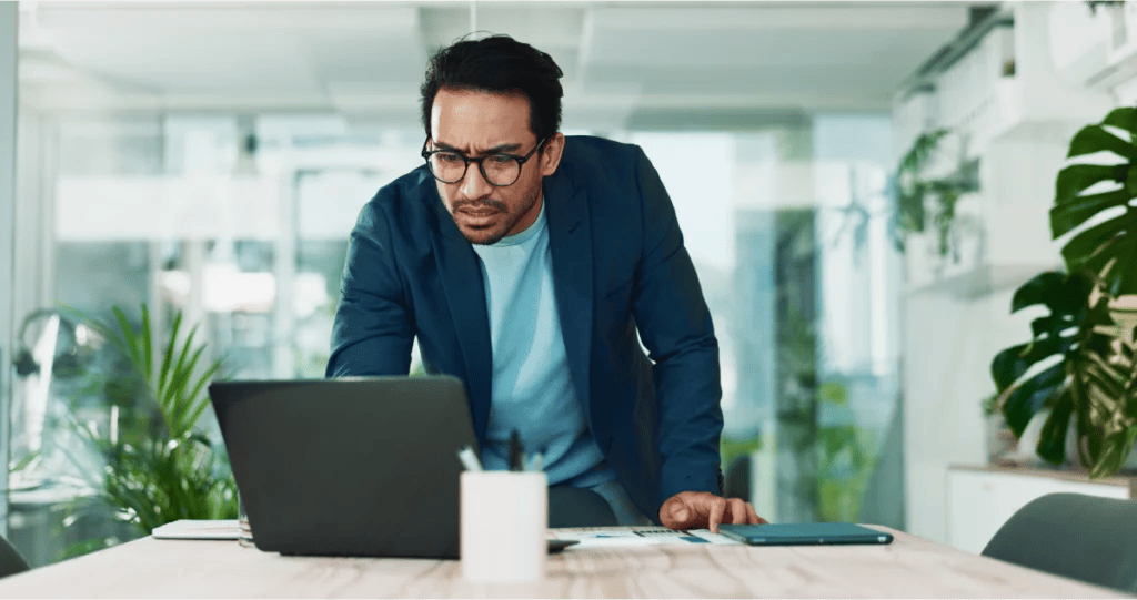 Concerned business professional in an office looks at his laptop in confusion.