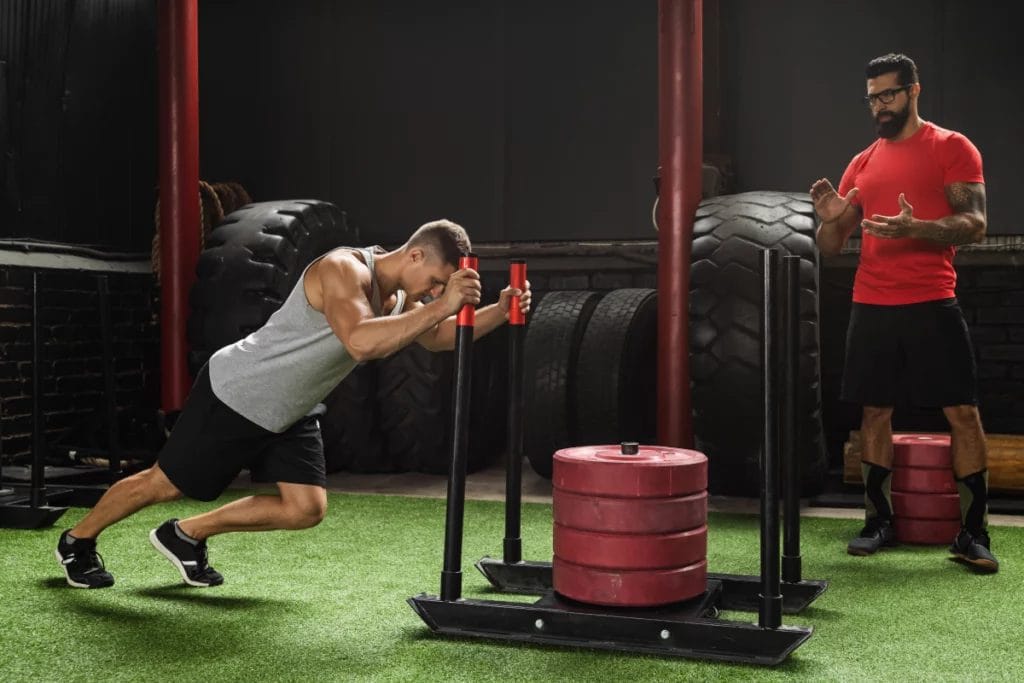 A personal trainer encourages a client pushing a weighted sled.
