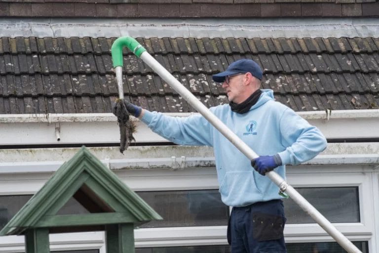 A man removing debris from a resident's gutter.