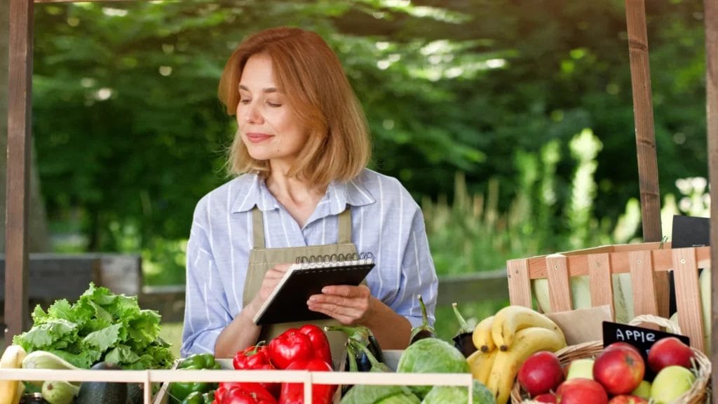 a female street vendor looking at a produce stand and writing in a notepad