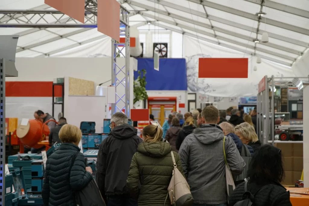 a group of event attendees wearing coats walking down an aisle packed with vendors