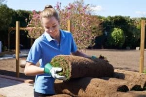 A female landscaper grabbing a roll of turf.