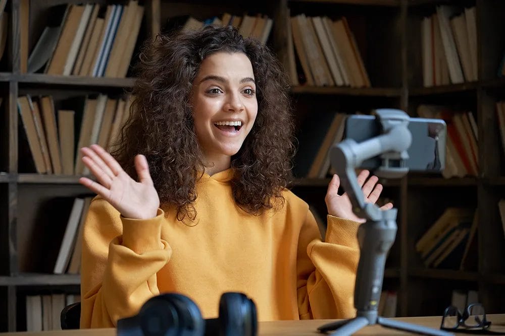 Woman recording a video with a camera, tripod, and headphones in a library