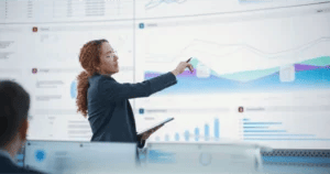 Consultant points to a graph and data on a large screen behind her