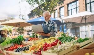 A farmers market vendor uses a laptop at his outdoor stall.