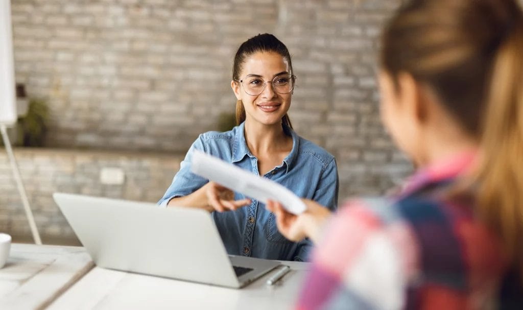 A business owner happily extends their hand to receive their documents back from a potential partner who was reviewing the papers.