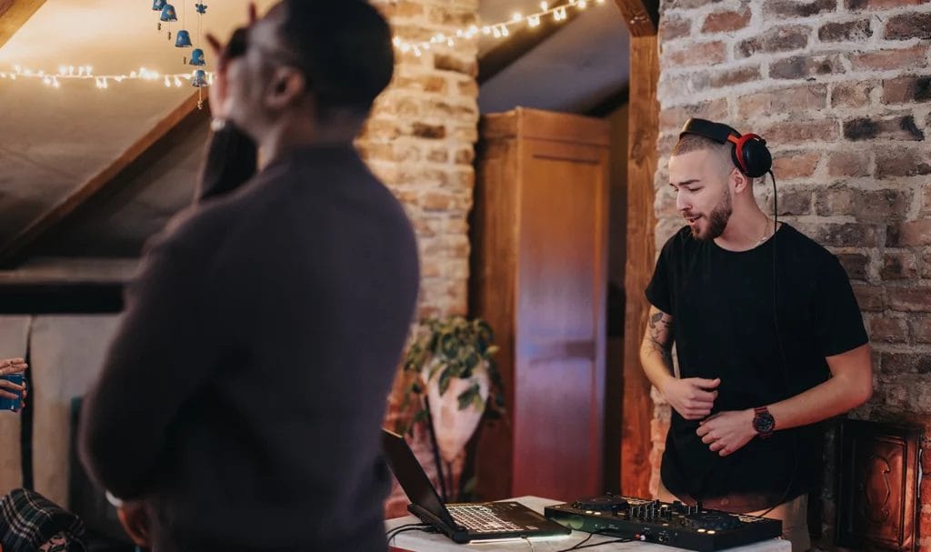 A DJ queues up his next song at a small indoor gathering where the crowd is enjoying the music.