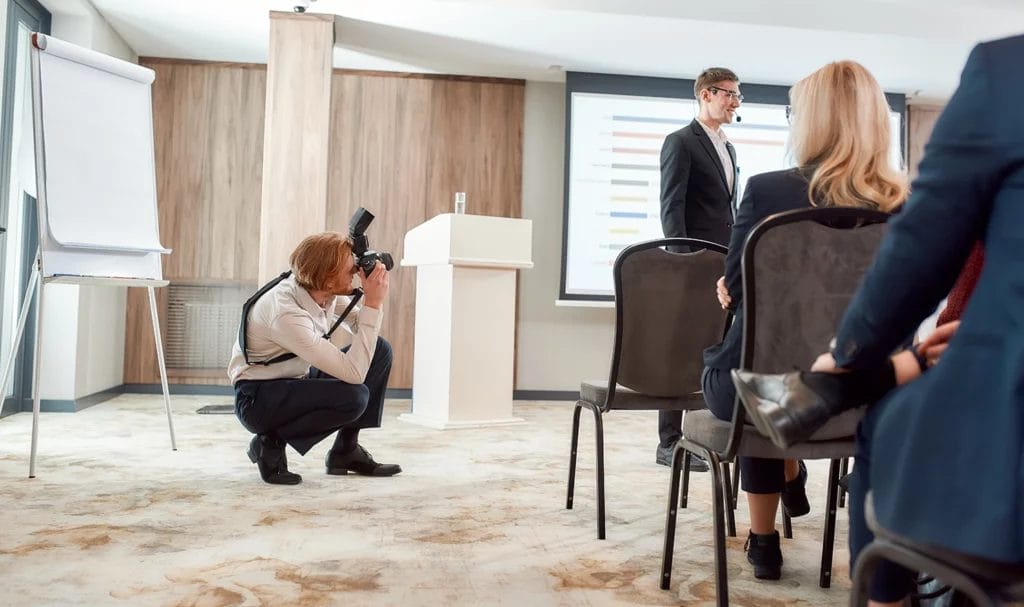A photographer kneels down to get the perfect shot of a speaker at a professional event.