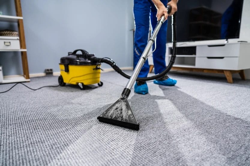 a person cleaning a carpet with a carpet cleaning wand while wearing blue shoe covers