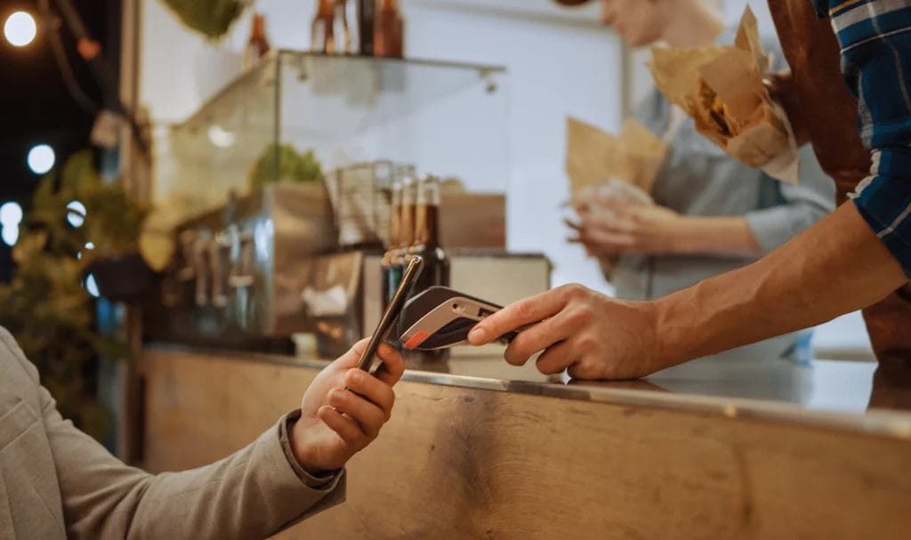 A close-up look at a customer using tap-to-pay on a digital payment kiosk held out by the food truck owner.