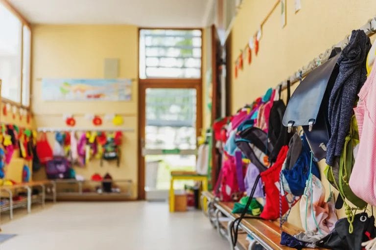 A bright yellow hallway at an elementary school with backpacks and coats hanging on coat racks and colorful posters on the walls.