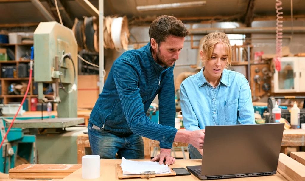 A business owner and employee work on a laptop inside their workspace.