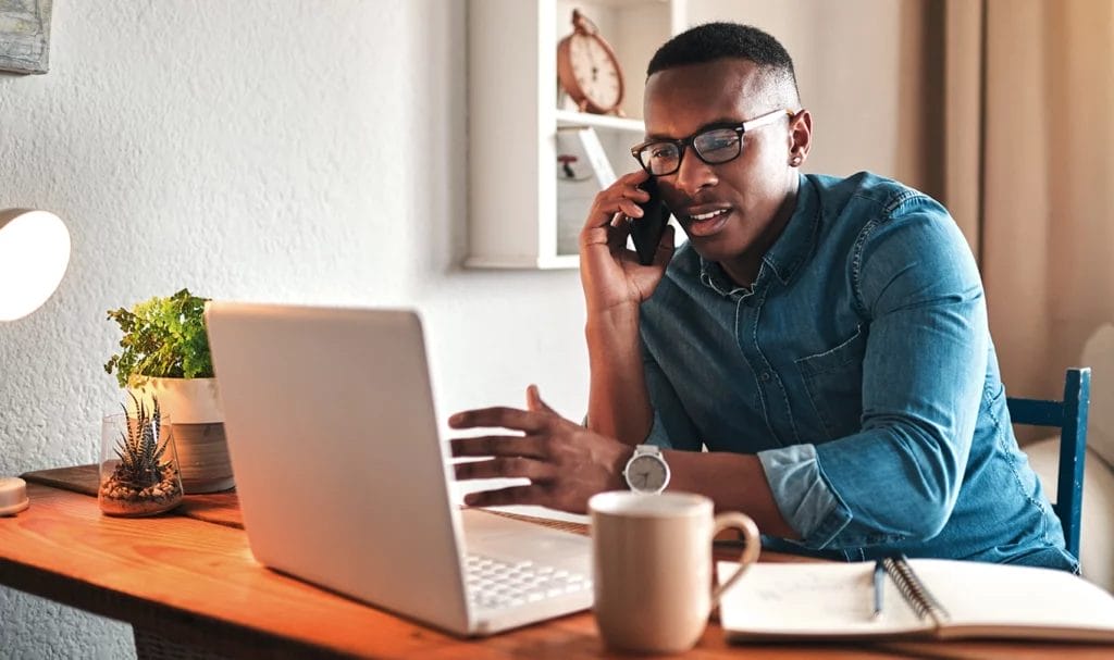 A consultant speaks to a client over the phone while working on a laptop in a home office.