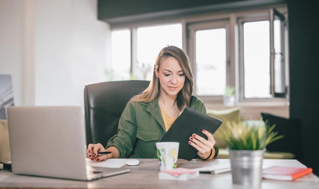 A small business owner using a tablet and a laptop in an office space.