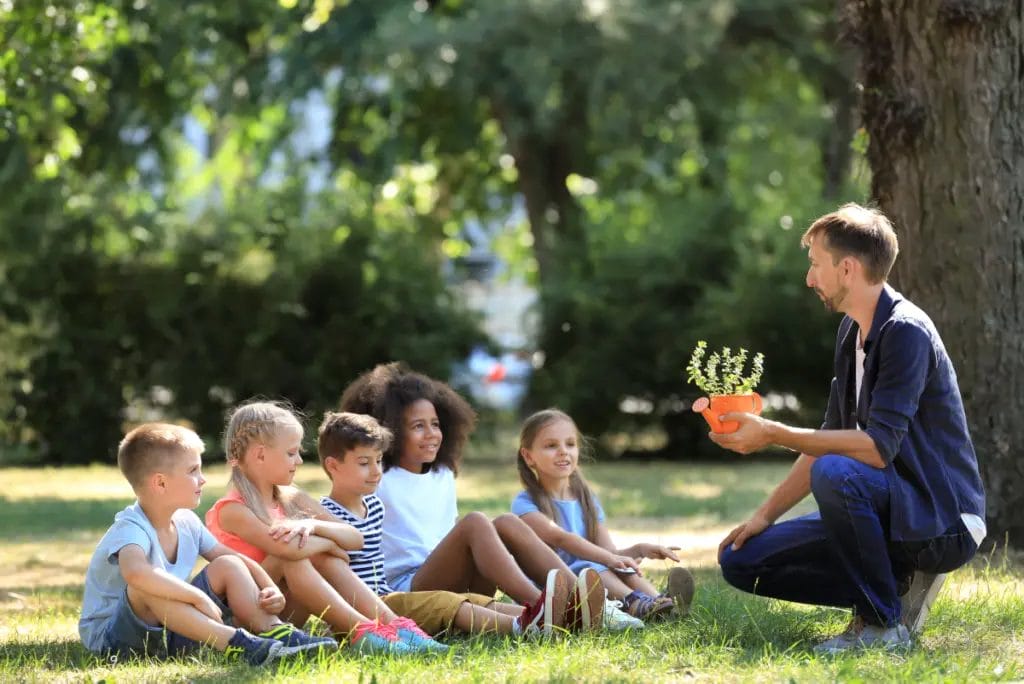 Teacher on a field trip with young students in outdoors explains biology
